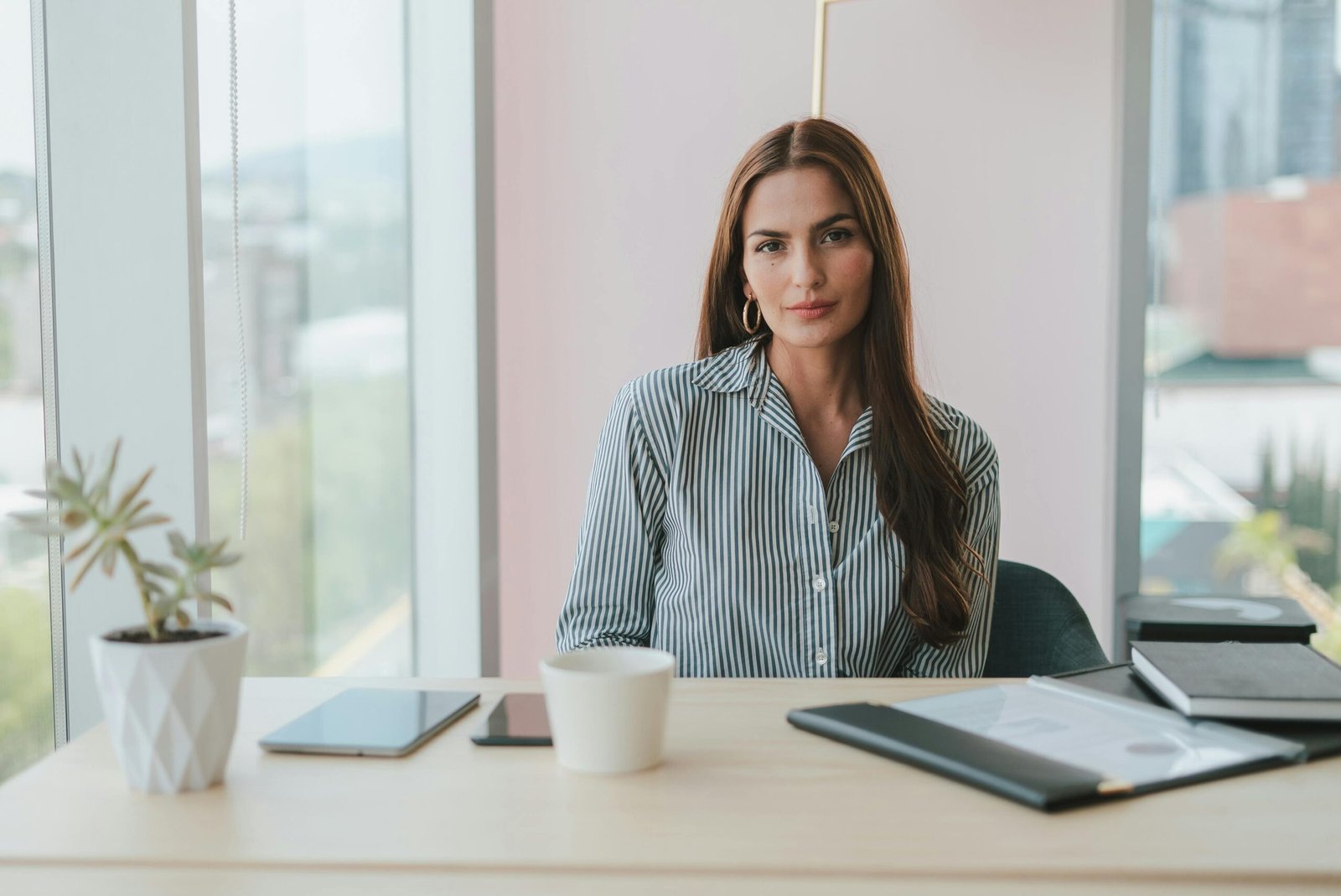Portrait of a businesswoman with brown hair sitting at a desk in a modern office environment.